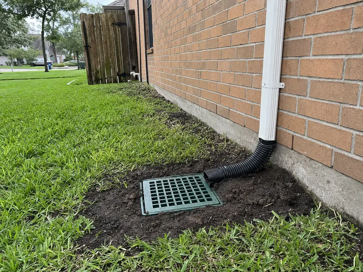 Catch basin grate set in a lawn beside a home's foundation